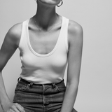 Person wearing a white tank top and high-waisted jeans against a plain background