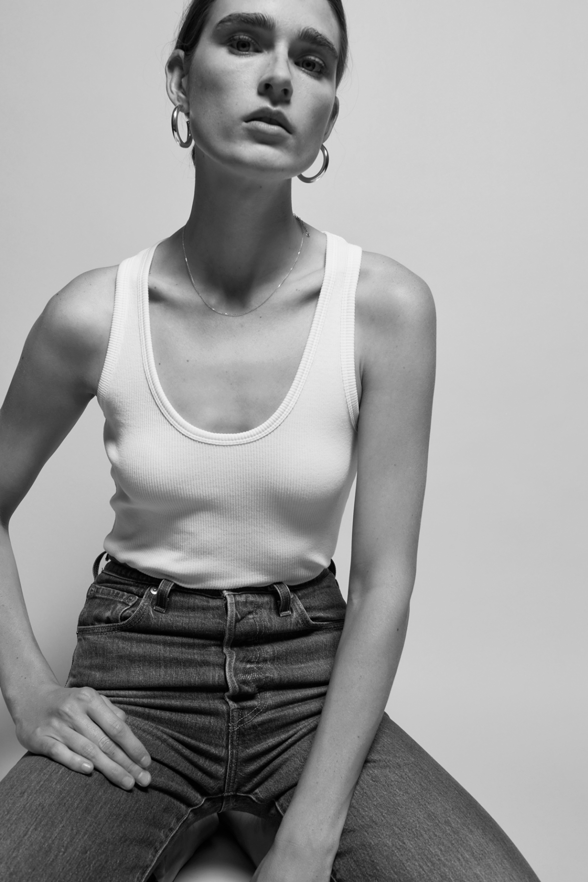 Person wearing a white tank top and high-waisted jeans against a plain background