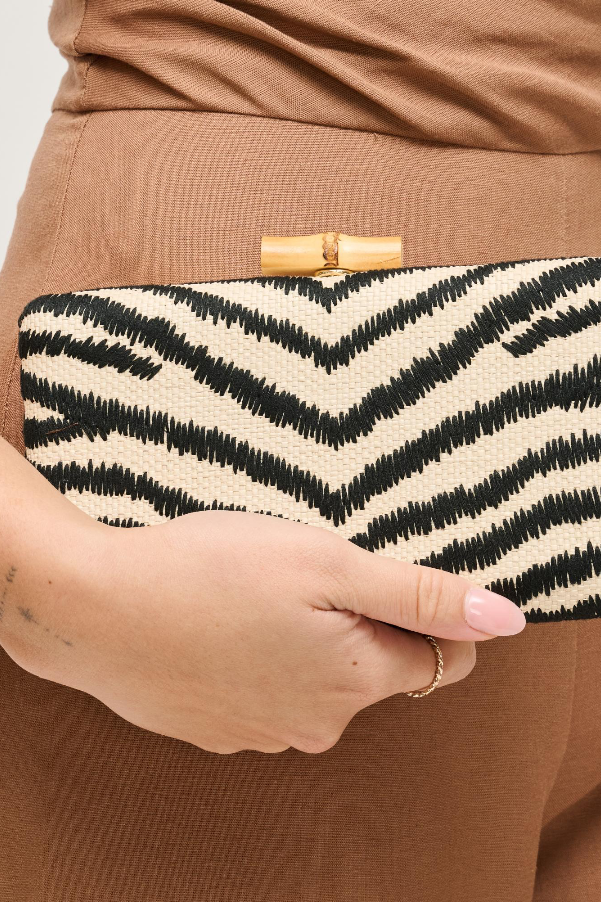 Clutch bag with zebra pattern held by a person wearing brown pants.