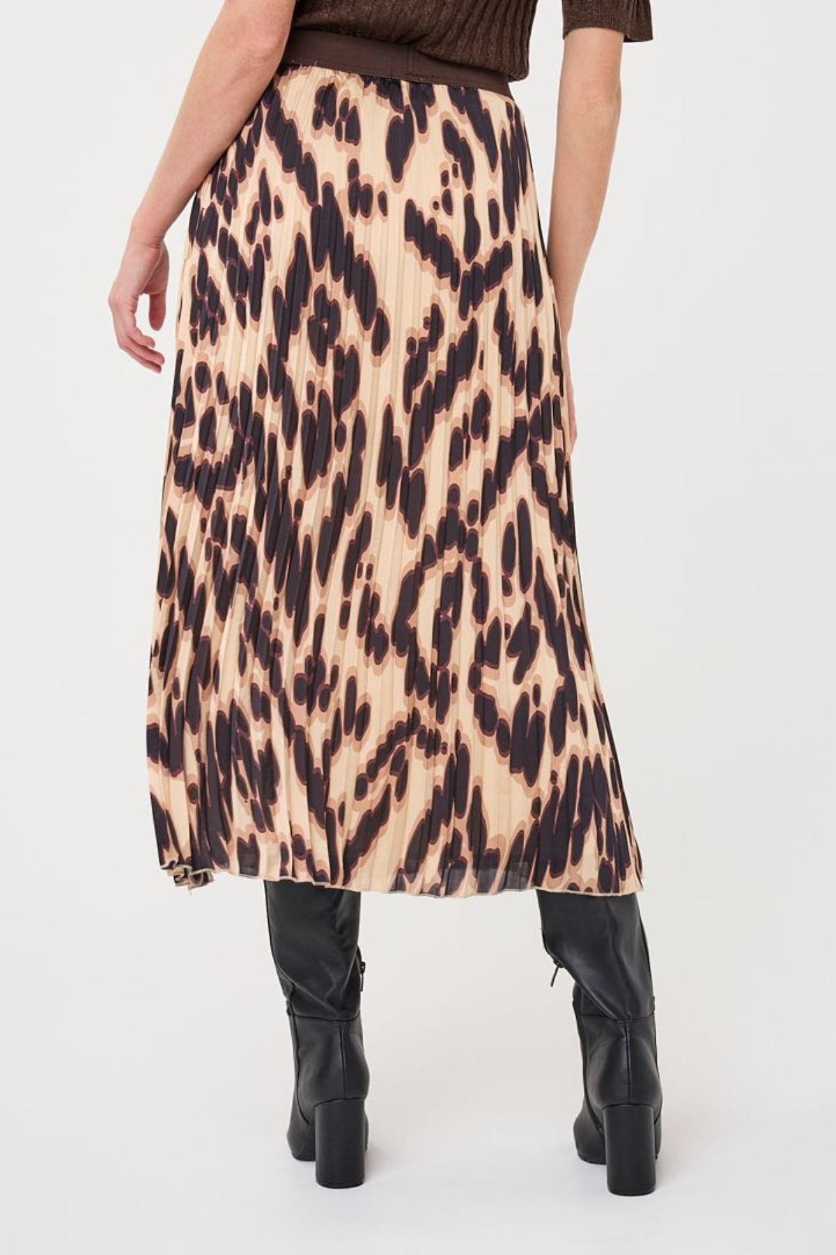 A model from the back wearing a pleated midi skirt with a leopard print pattern in beige, brown, and black, paired with black heeled boots against a white studio background.