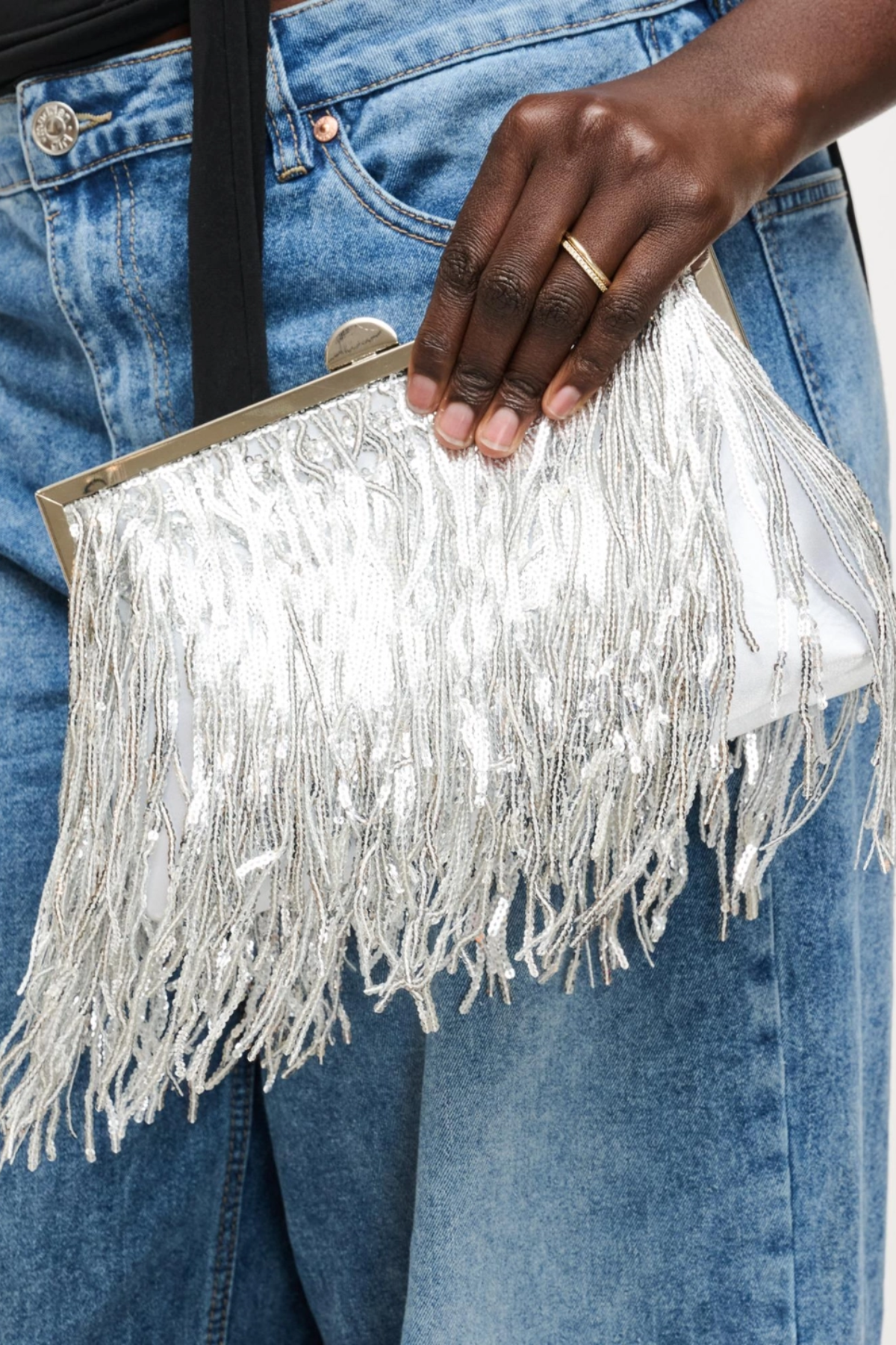 Silver fringe clutch held by a person wearing blue jeans
