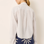 A woman shown from the back wearing a white long-sleeve button-up shirt with thin vertical navy stripes and a navy mini skirt with white embroidered details, against a plain beige background.