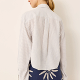 A woman shown from the back wearing a white long-sleeve button-up shirt with thin vertical navy stripes and a navy mini skirt with white embroidered details, against a plain beige background.