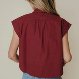 A woman shown from behind wearing a sleeveless, deep burgundy top and light blue jeans against a plain beige background.
