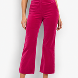A model wearing bright fuchsia pink velvet cropped flare pants, paired with a white ribbed top and white heeled sandals, standing against a white studio background.