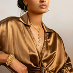 Woman wearing a gold satin shirt with jewelry against a neutral background