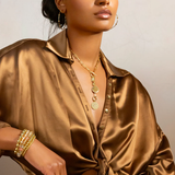 Woman wearing a gold satin shirt with jewelry against a neutral background
