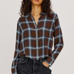 A woman modeling a brown, blue, and white plaid button-up shirt with dark wash jeans, photographed against a solid light gray background.