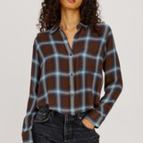 A woman modeling a brown, blue, and white plaid button-up shirt with dark wash jeans, photographed against a solid light gray background.