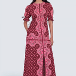 A model wearing a long-sleeved maxi dress with a pink and burgundy paisley pattern, standing against a light gray studio background.