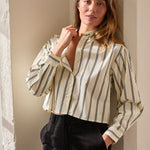 Woman wearing a striped blouse and black pants against a neutral wall.