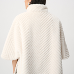 Person wearing a cream-colored knitted poncho against a white background