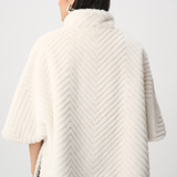Person wearing a cream-colored knitted poncho against a white background