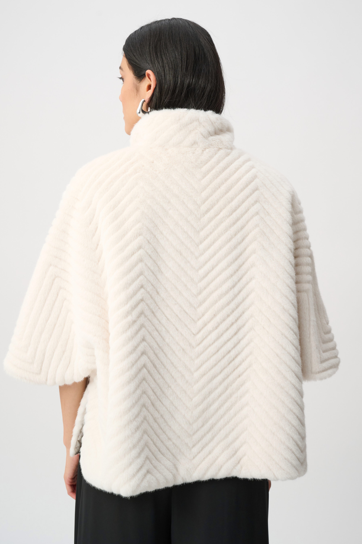 Person wearing a cream-colored knitted poncho against a white background