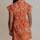 Woman wearing a floral dress with orange and pink pattern on a plain background