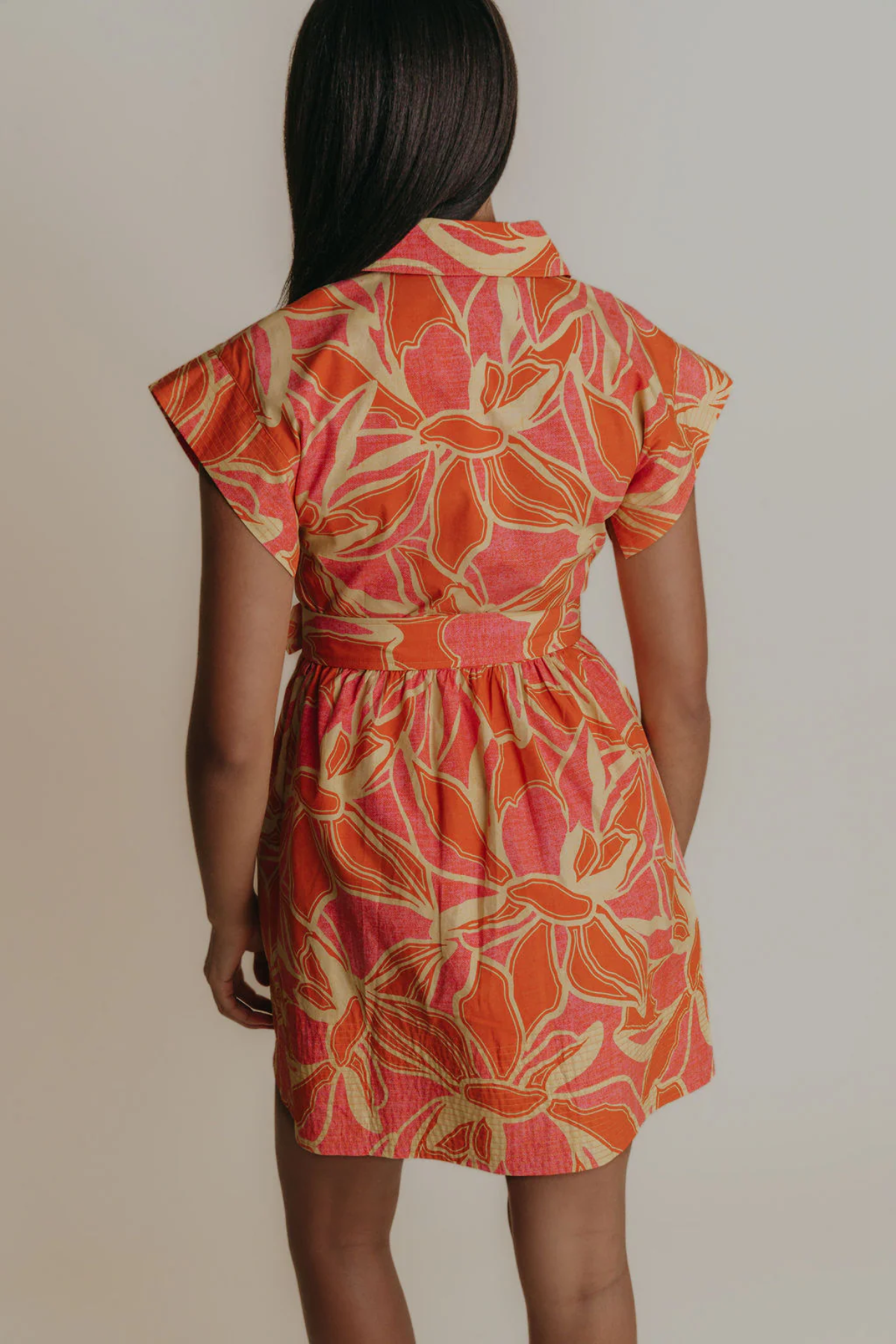 Woman wearing a floral dress with orange and pink pattern on a plain background