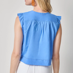 Woman wearing a blue sleeveless top with ruffled shoulders on a plain background