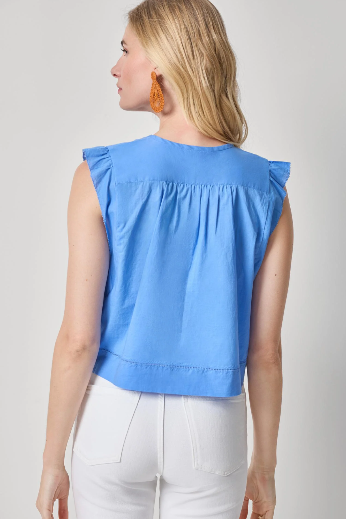 Woman wearing a blue sleeveless top with ruffled shoulders on a plain background
