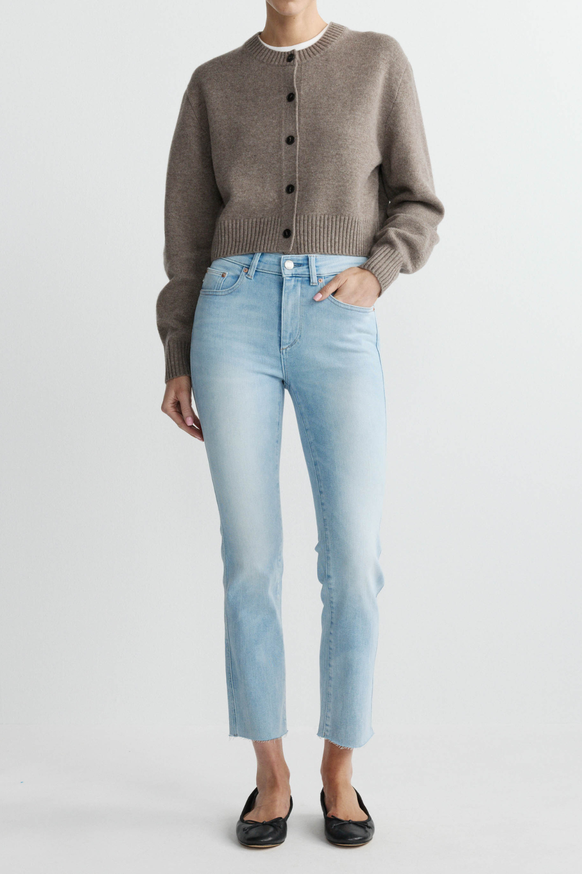 Person wearing a brown cardigan, light blue jeans, and black shoes on a white background