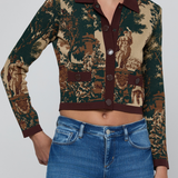A cropped long-sleeve button-front cardigan with a dark green and beige toile-style print, worn by a model with blue jeans against a light gray studio background.