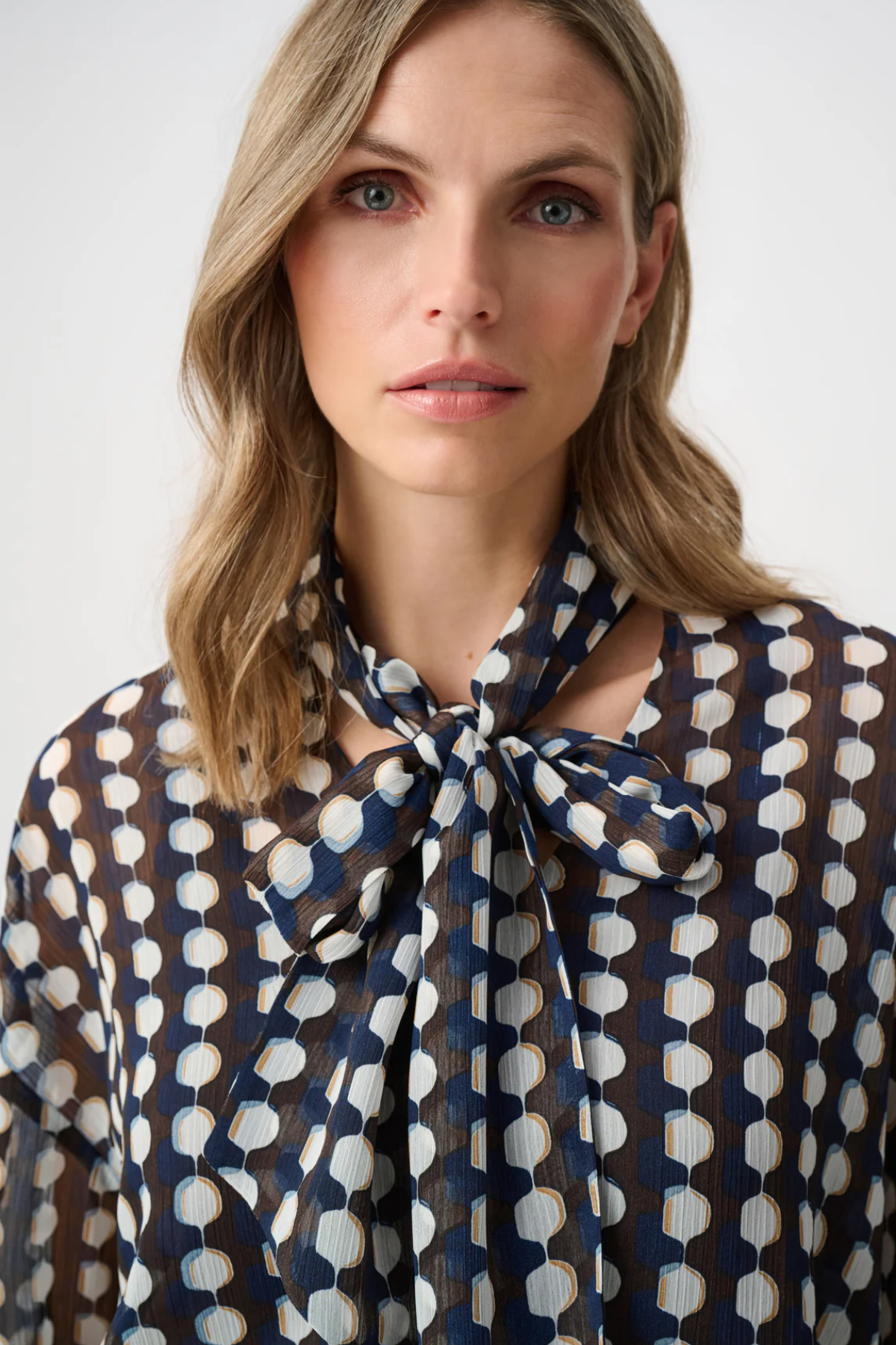 Model wearing a long-sleeve chiffon blouse with a geometric print and tie-neck detail in a relaxed, feminine silhouette.