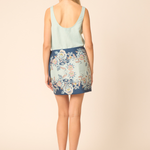 Woman wearing a light blue sleeveless top and floral skirt on a beige background