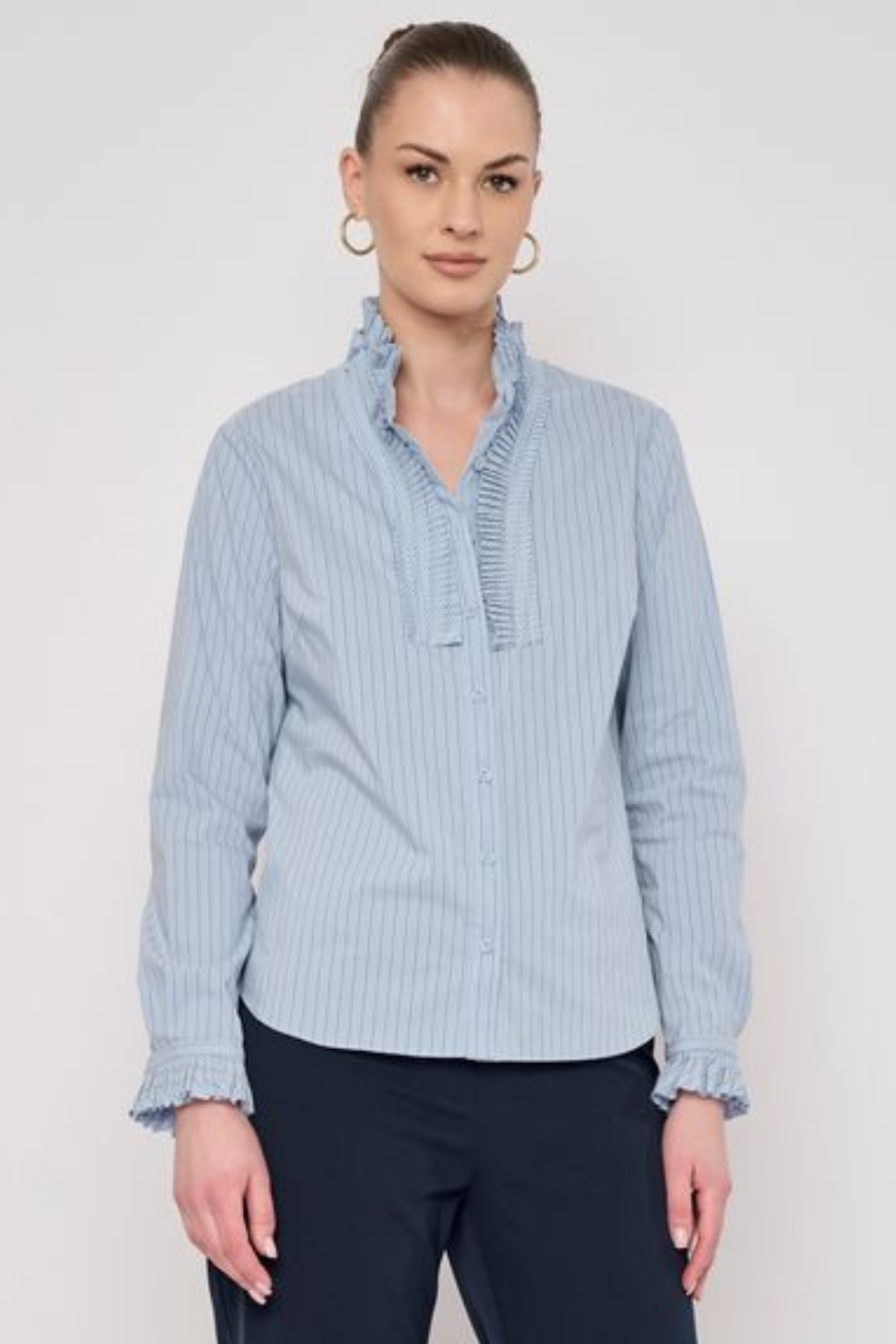 Model wearing a striped long-sleeve blouse with ruffle detailing and a relaxed, polished silhouette.