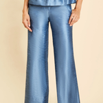 A model wearing a pair of wide-leg blue trousers with a subtle sheen, paired with a matching blue peplum top and metallic sandals, set against a solid beige background.