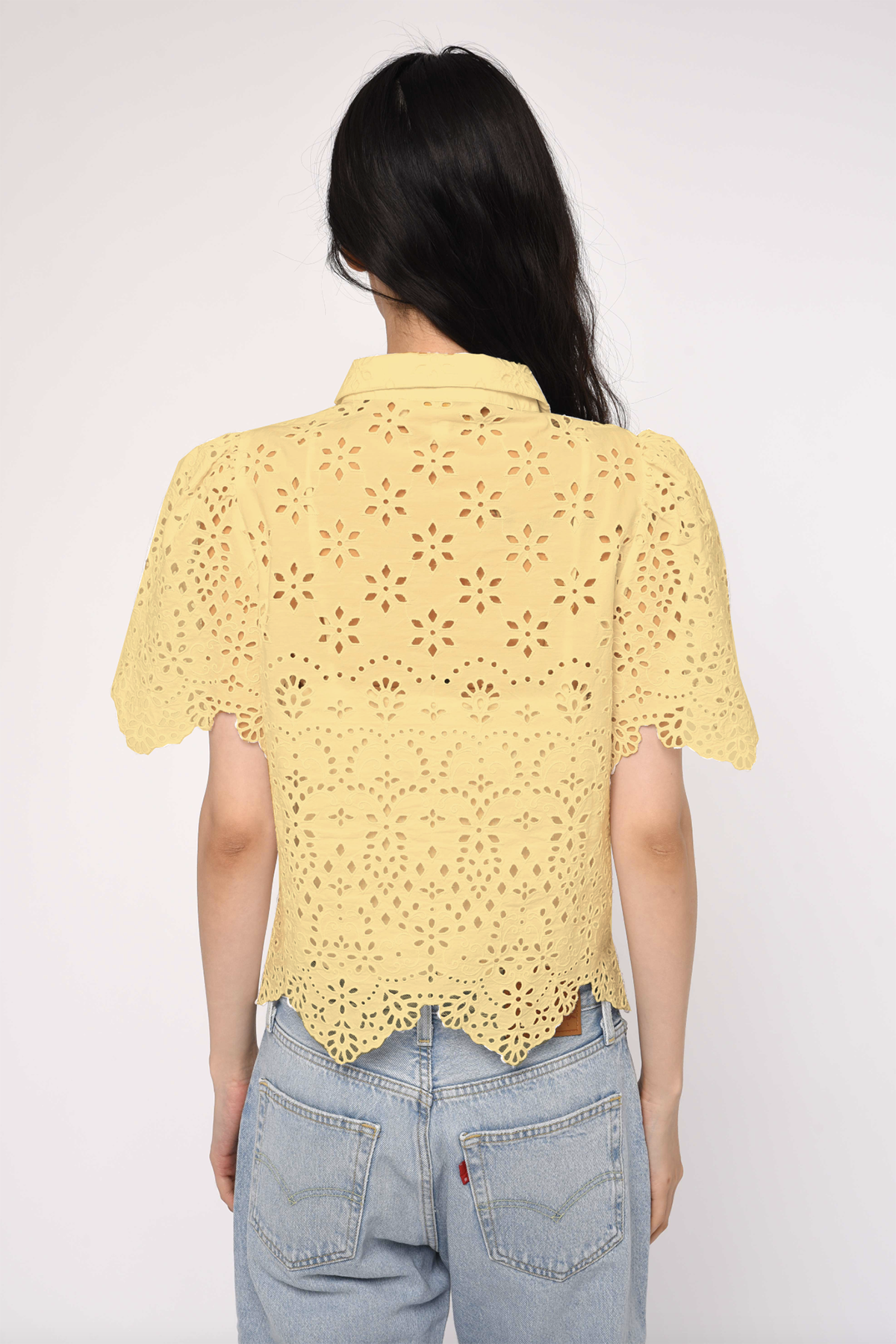 Person wearing a yellow lace top and blue jeans on a white background