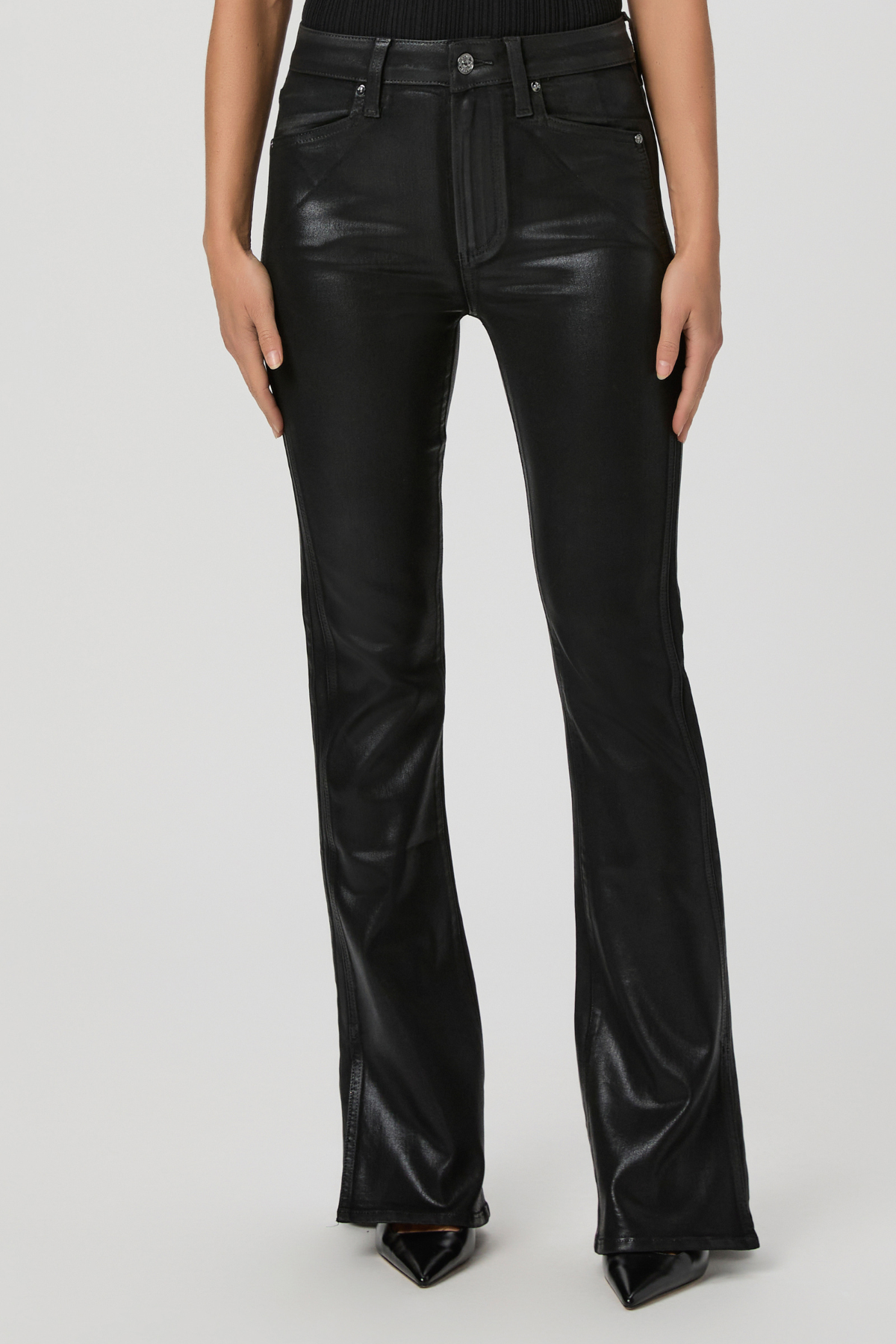 Black faux-leather flare jeans with a glossy finish, modeled on a person wearing black pointed-toe heels against a light gray studio background.