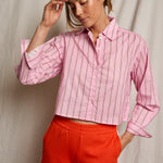 Woman wearing a pink striped shirt and red pants against a neutral background