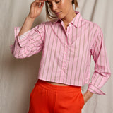 Woman wearing a pink striped shirt and red pants against a neutral background
