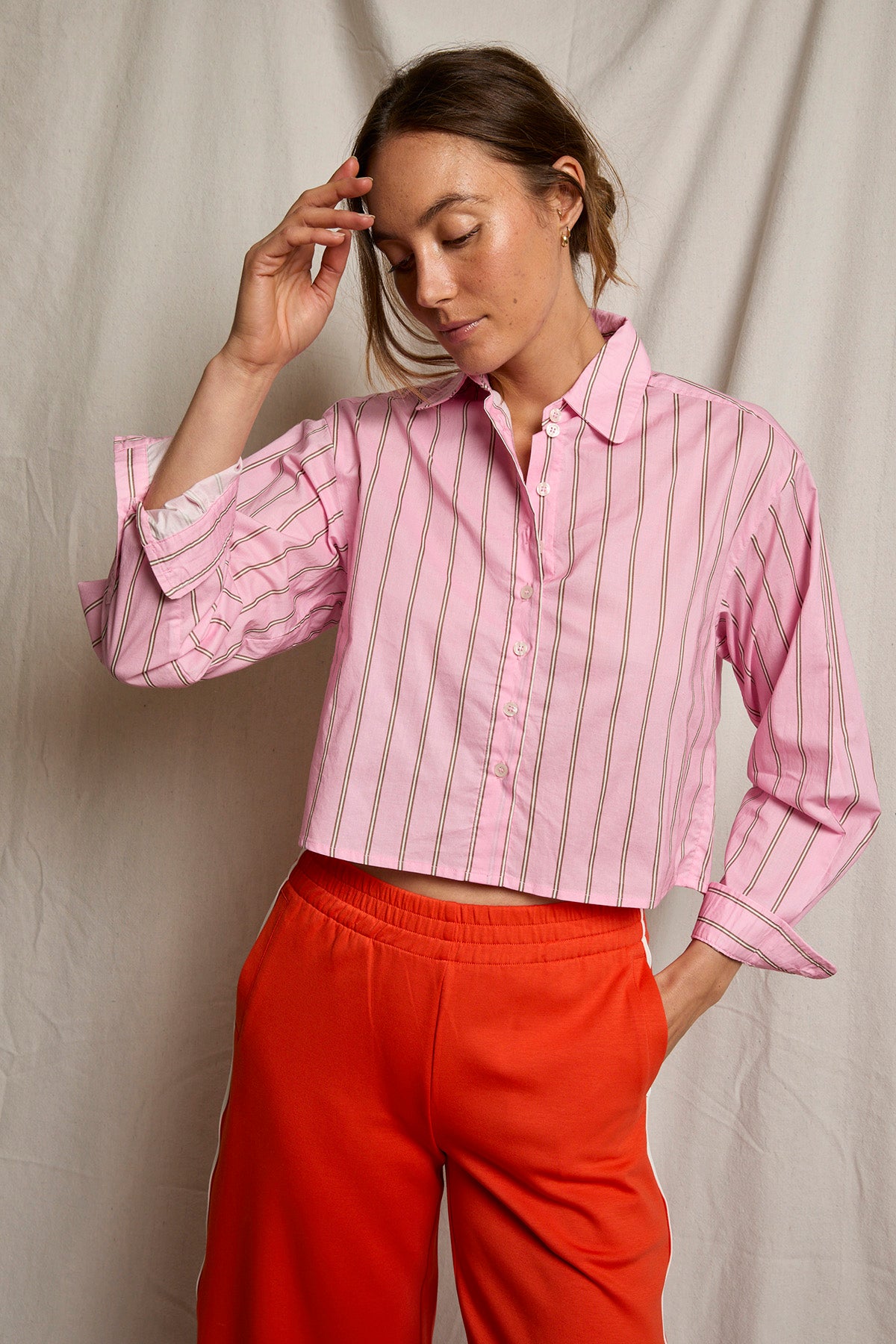 Woman wearing a pink striped shirt and red pants against a neutral background
