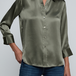 Model wearing dark green blouse with jeans on off white background.