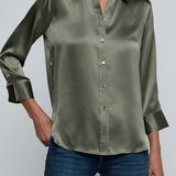 Model wearing dark green blouse with jeans on off white background.