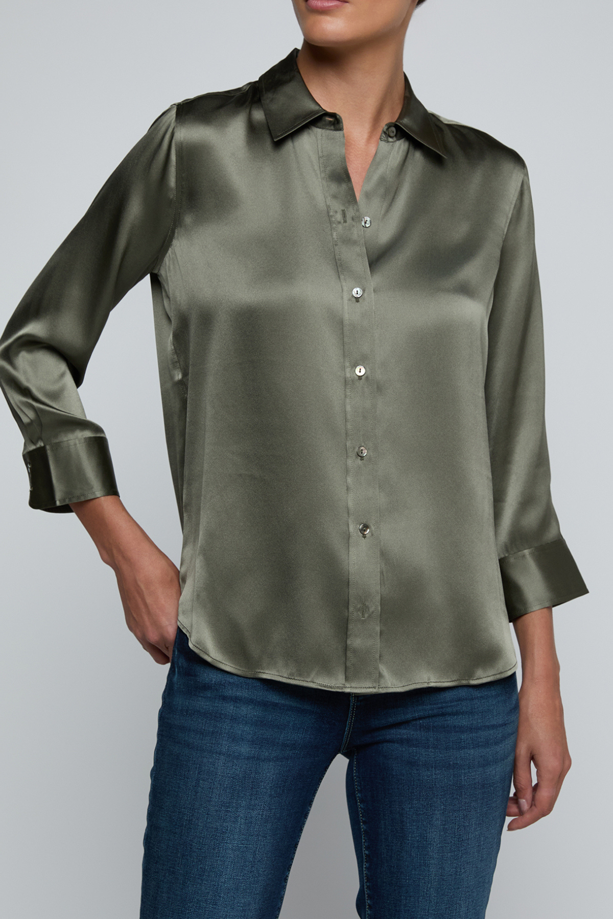 Model wearing dark green blouse with jeans on off white background.