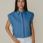 Woman wearing a blue sleeveless blouse with scalloped edges against a plain background
