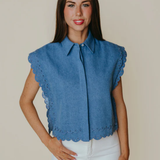 Woman wearing a blue sleeveless blouse with scalloped edges against a plain background