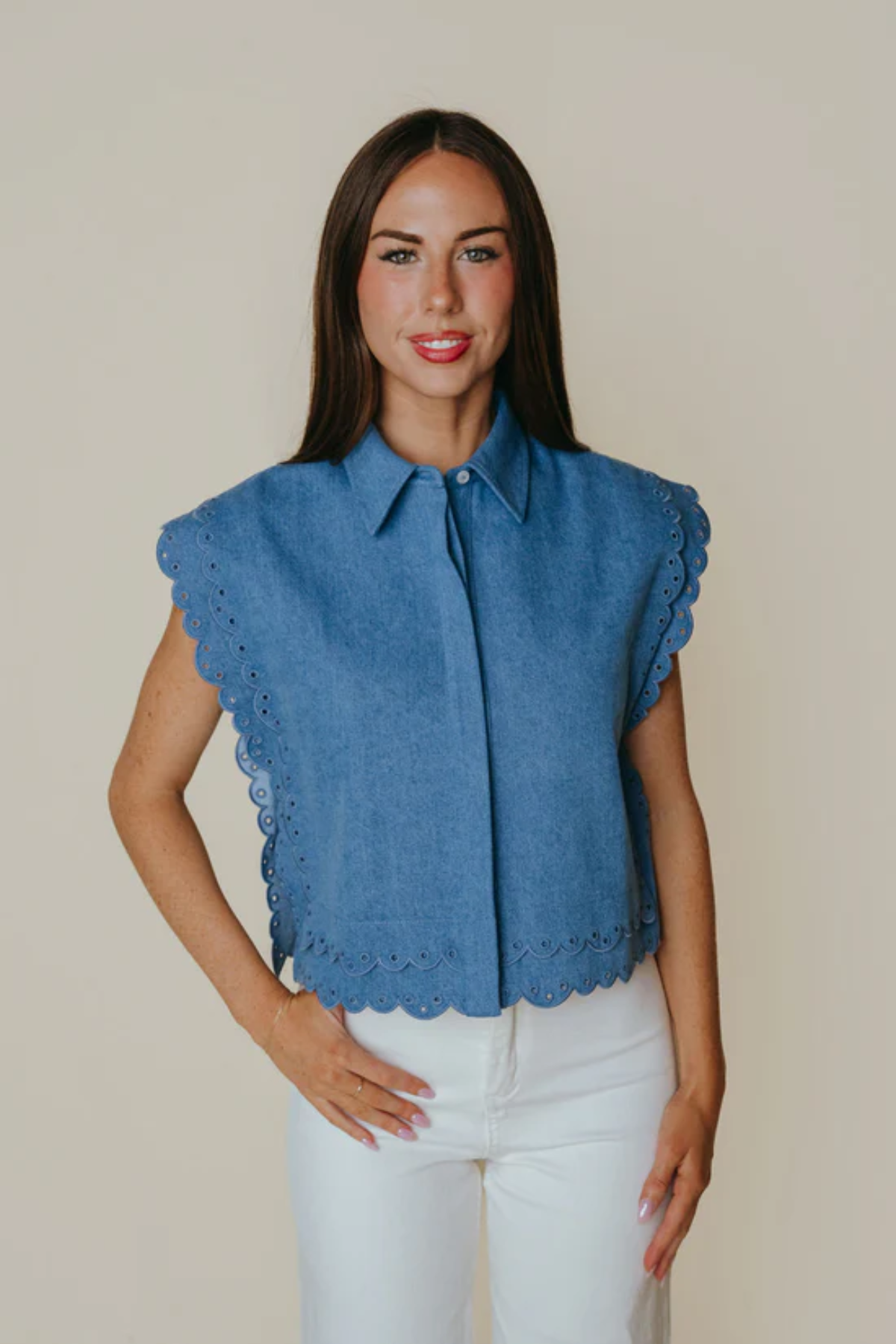 Woman wearing a blue sleeveless blouse with scalloped edges against a plain background