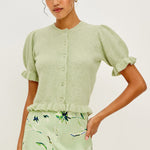 Woman wearing a light green cardigan and floral skirt on a white background