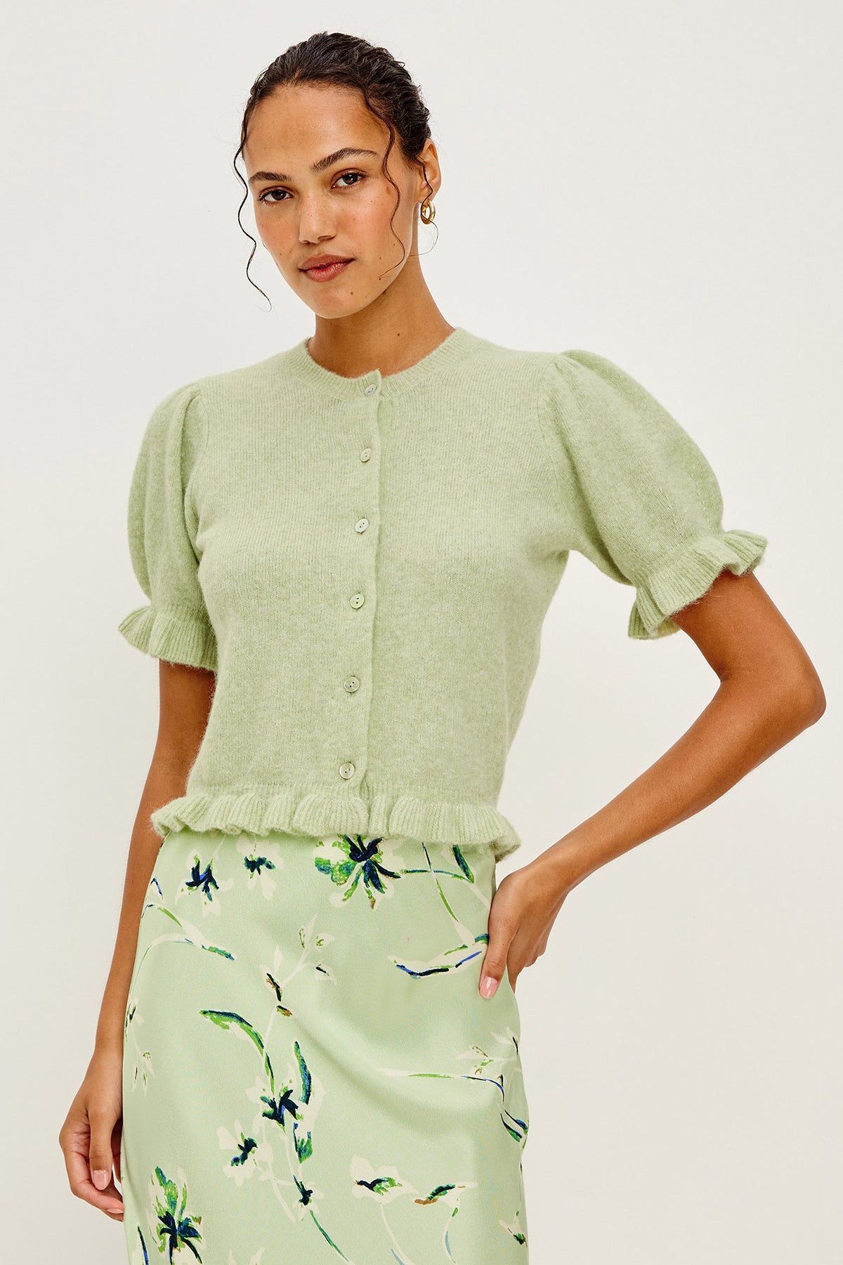 Woman wearing a light green cardigan and floral skirt on a white background