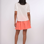 Person wearing a white top and coral skirt on a white background