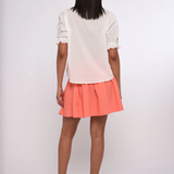 Person wearing a white top and coral skirt on a white background
