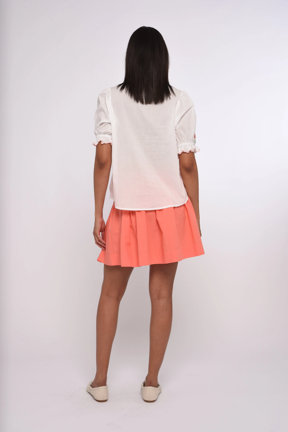 Person wearing a white top and coral skirt on a white background