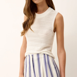 Woman wearing a white sleeveless top and striped pants on a plain background