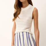 Woman wearing a white sleeveless top and striped pants on a plain background