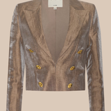 A cropped double-breasted blazer in a metallic bronze fabric with gold buttons, shown flat against a solid beige background. The brand label 'L'AGENCE' is visible at the collar.