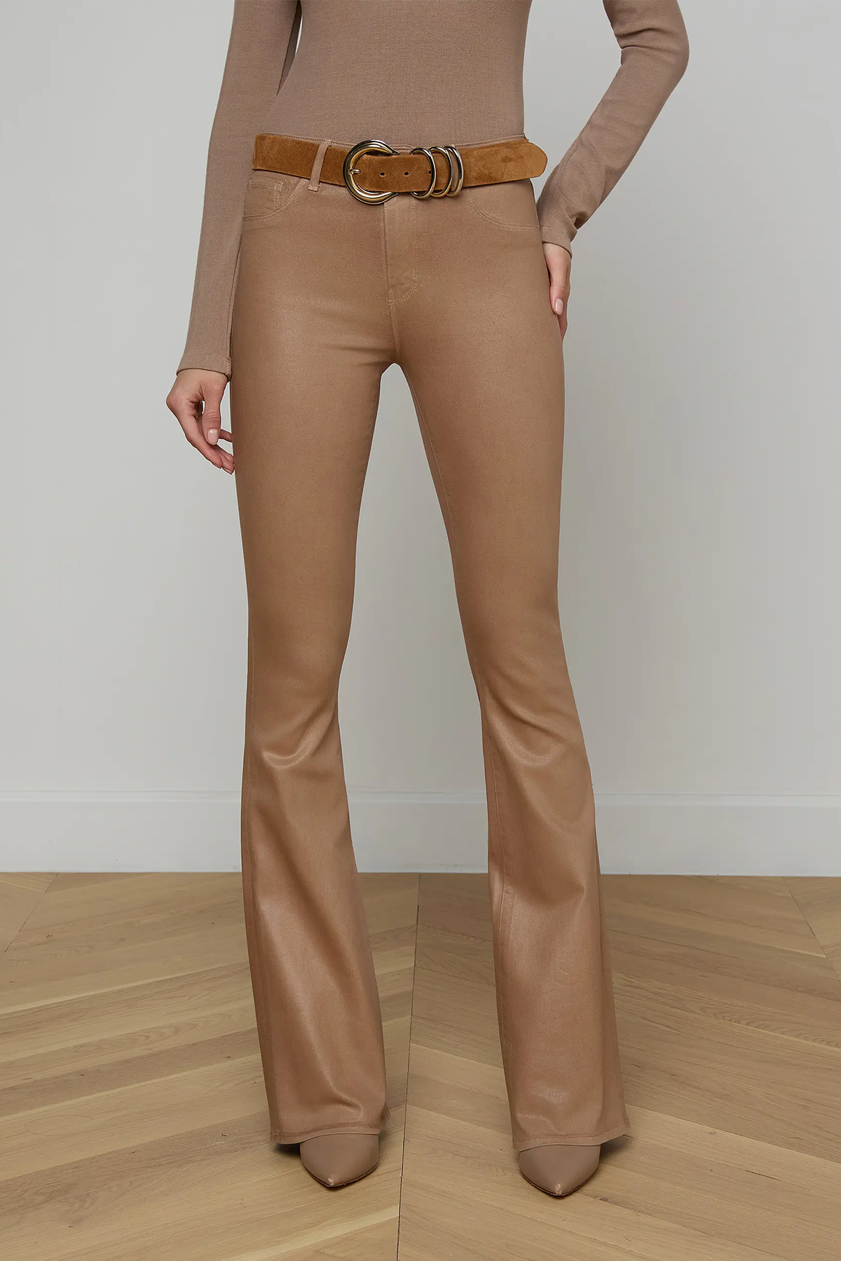 Person wearing brown flared pants and a matching top on a wooden floor with a white wall background.