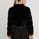 Woman wearing a black faux fur jacket and leopard print skirt on a plain background