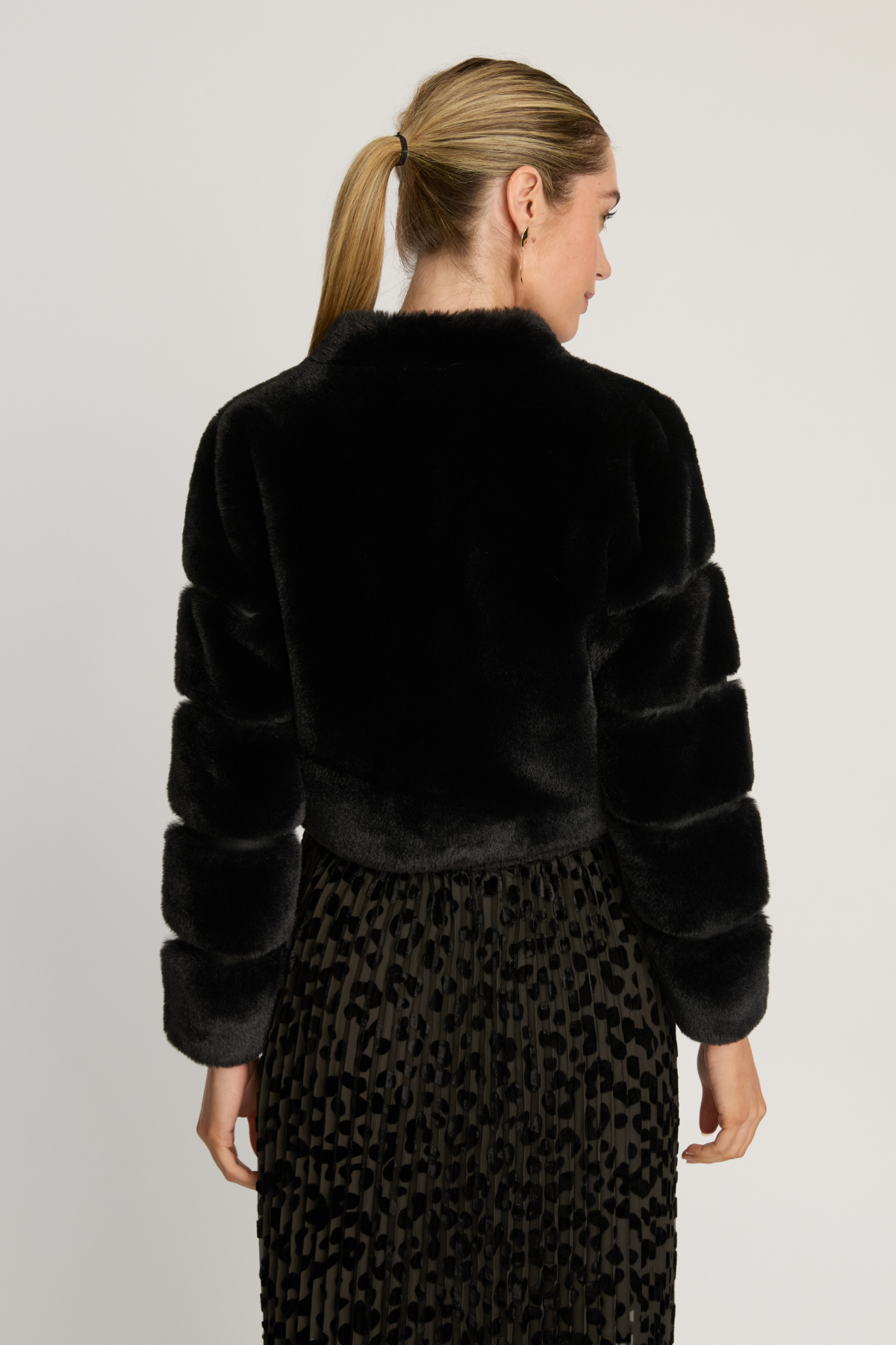 Woman wearing a black faux fur jacket and leopard print skirt on a plain background